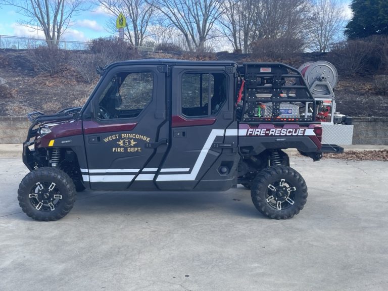 A red and black off-road fire rescue vehicle from West Buncombe Fire Department, labeled "Fire-Rescue" on the side. It has a number 35 on the door and is equipped with firefighting equipment at the back. The vehicle is parked outdoors on a concrete surface.