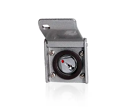 Close-up of a small, rectangular, metallic device with a circular hole in the center, mounted on a flat base with a small bracket extending upwards. The device has a reflective interior and is secured with screws at the corners.