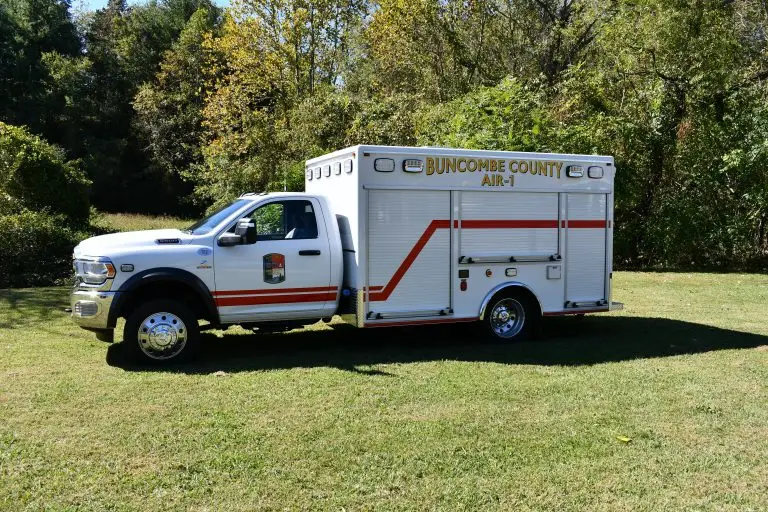 A Buncombe County emergency response vehicle labeled "AIR-1" is parked on a grassy area. The truck is white with red stripes and trees are visible in the background.