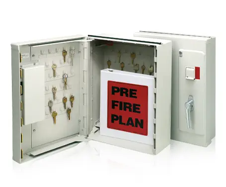 Two white metal key cabinets are shown. One is closed and features a lock and handle, while the other is open, displaying numerous keys hanging inside and a red folder labeled "PRE FIRE PLAN." The cabinets are used for secure key storage and emergency plans.