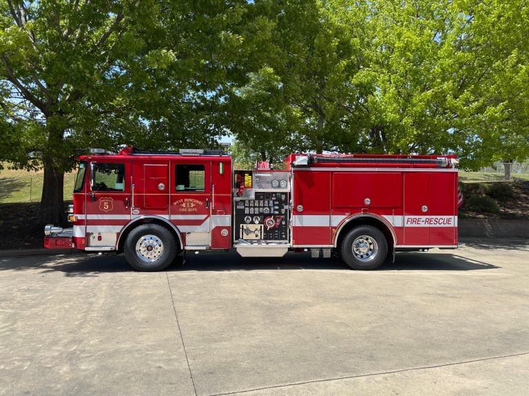 A bright red fire-rescue truck marked "Engine 5" is parked on a paved surface, with green trees in the background on a sunny day.