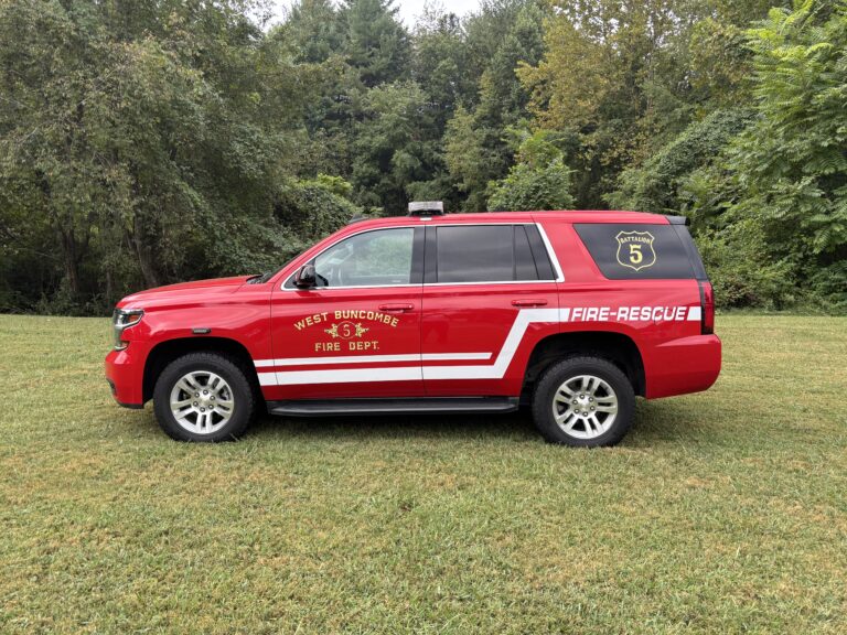 A red West Buncombe Fire Dept. SUV marked “FIRE-RESCUE” is parked on grass with trees in the background.